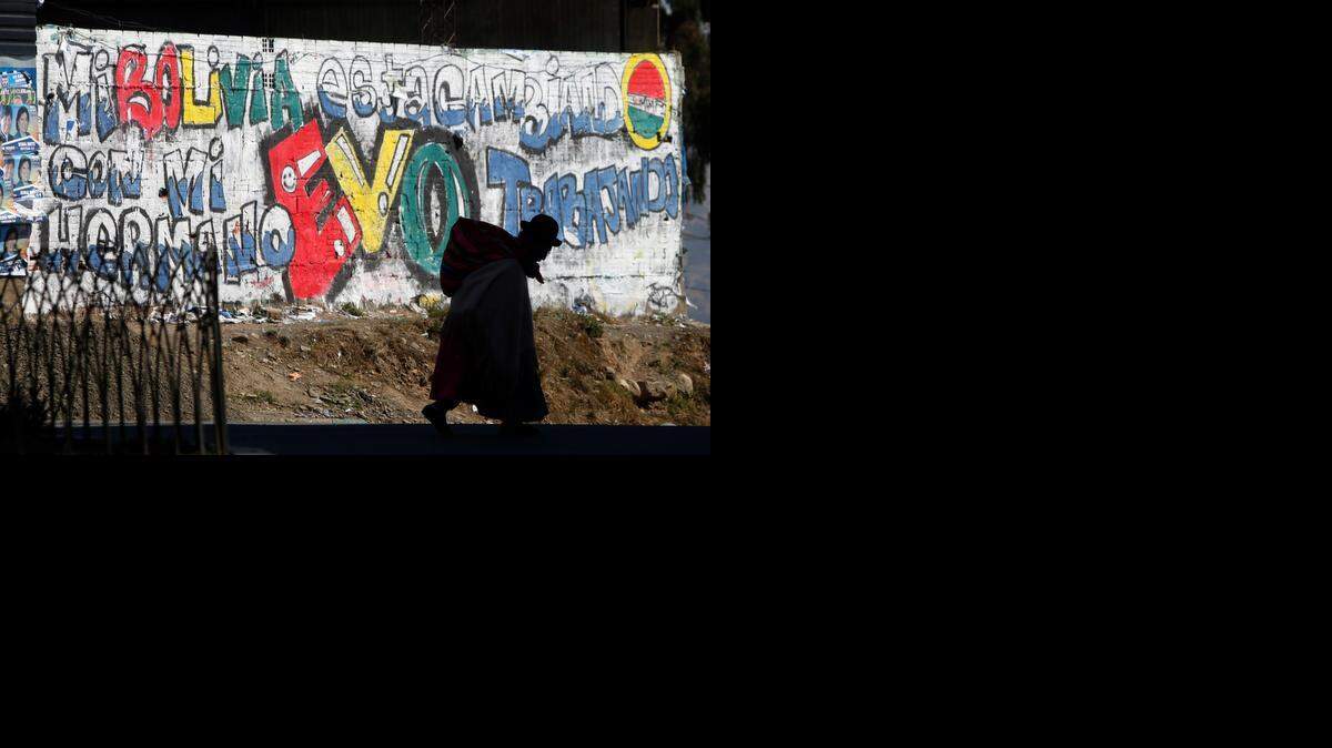
Una mujer cargando un bulto pasa frente a un letrero de apoyo a Evo Morales, en La Paz, Bolivia.
