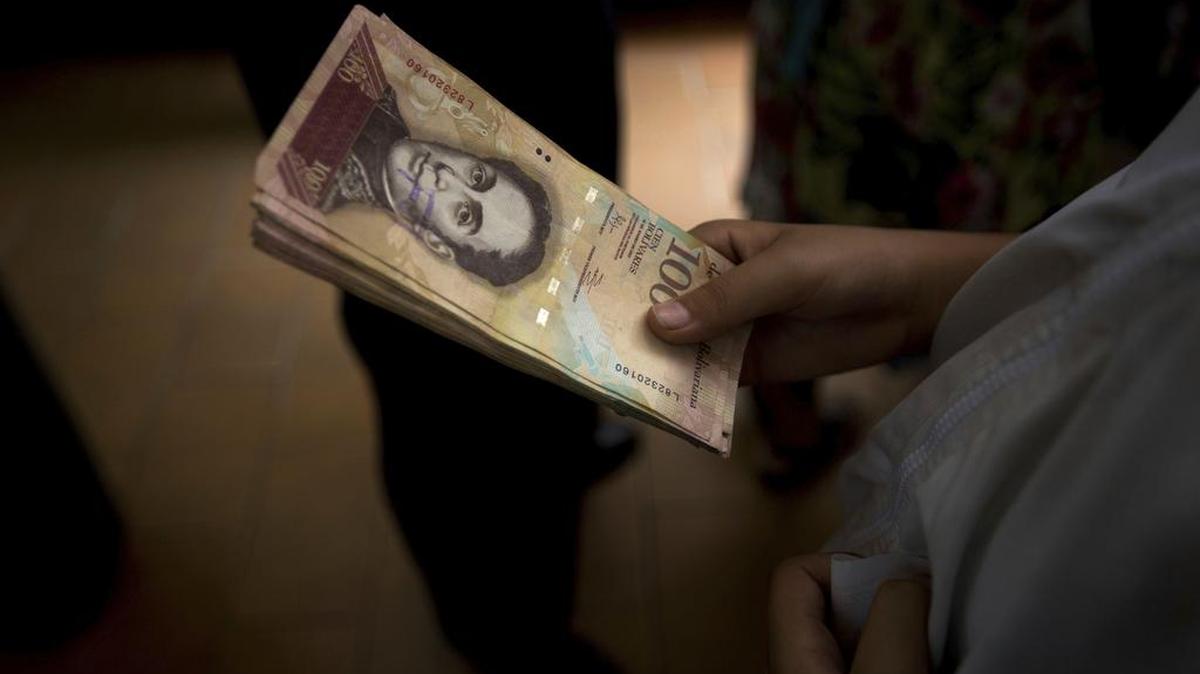 Un hombre sostiene un fajo de billetes de 100 bolívares en una panadería en el centro de Caracas, Venezuela. Foto de archivo.