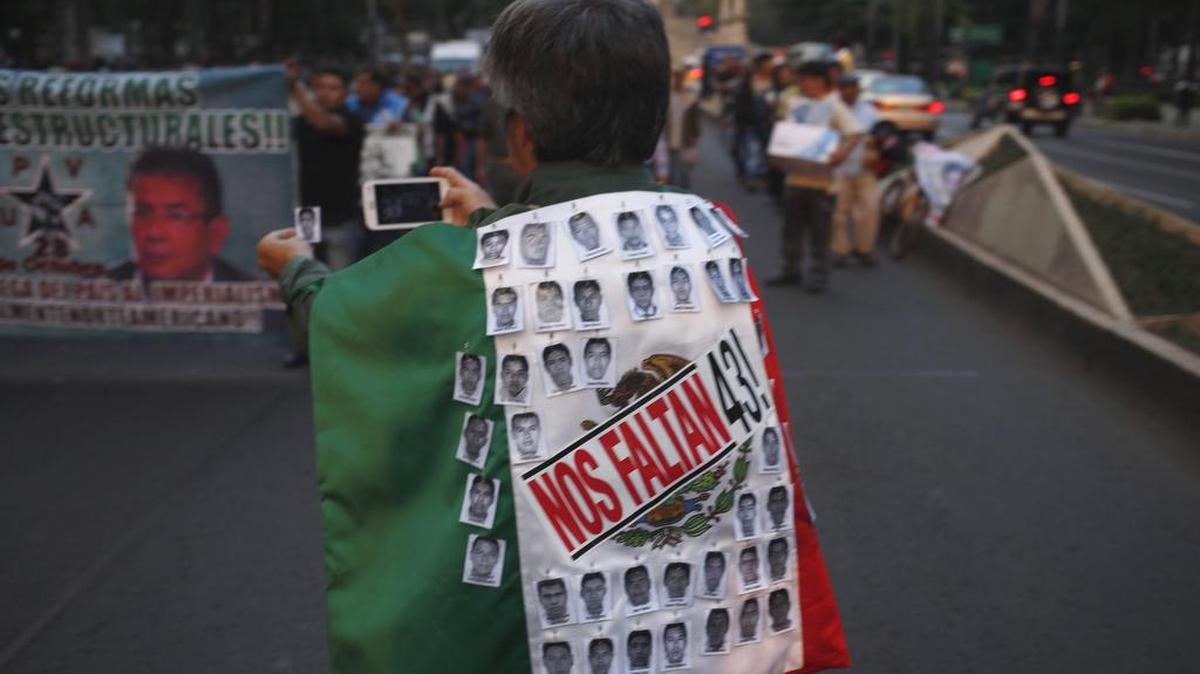 En esta foto de archivo, una persona hace una copia de una foto de un estudiante que falta mientras lleva una bandera mexicana con las fotos de los 43 estudiantes que desaparecidos con la frase: "Nos faltan 43", durante una marcha en la ciudad de México.