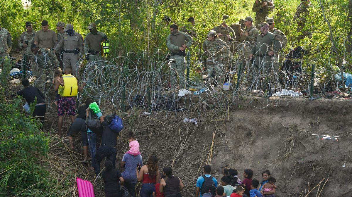 LA POLICIA estatal de Texas termina de colocar alambre de púas mientras los migrantes caminan por la orilla del río Bravo, visto desde Matamoros, México, el miércoles 10 de mayo de 2023.