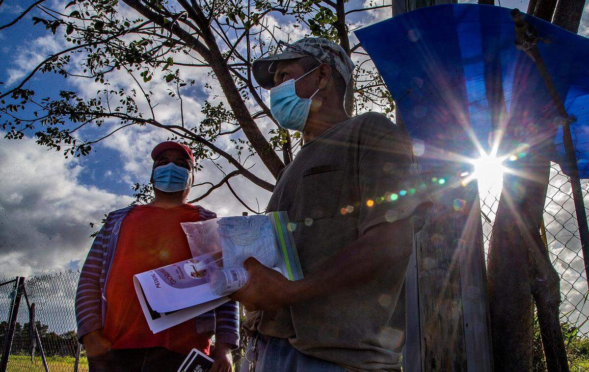 José Alfredo (right), a laborer (Jornalero) holds a flyer with information about workers rights and a kit including CDCs covid protection guidance, masks and hand sanitizer, handed out by Erick Sanchez, a workers rights organizer with WeCount!, a community organization defending the rights of day laborers, domestic workers, farmworkers, and plant nursery workers, based in Homestead. on Wednesday, March 10, 2021.