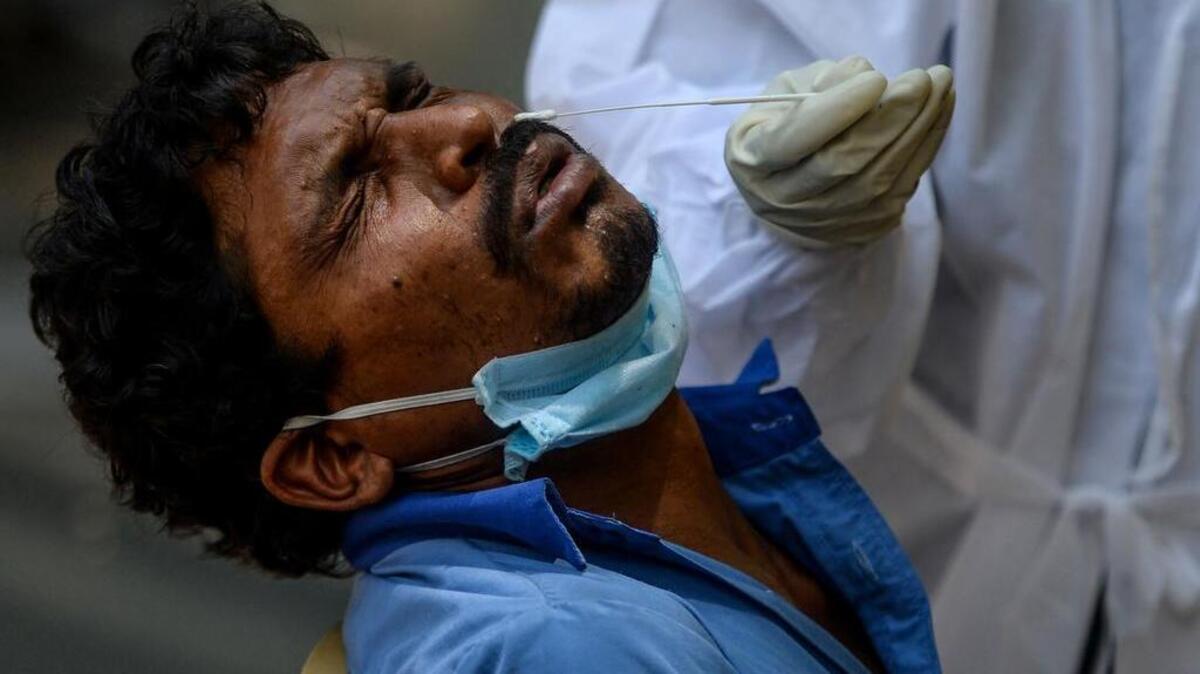 Un trabajador de la salud toma una muestra de un hisopo de un hombre que realiza la prueba de COVID-19 en un campo de pruebas en una zona de contención implementada como medida preventiva contra el coronavirus COVID-19 en Chennai el 30 de julio de 2020.