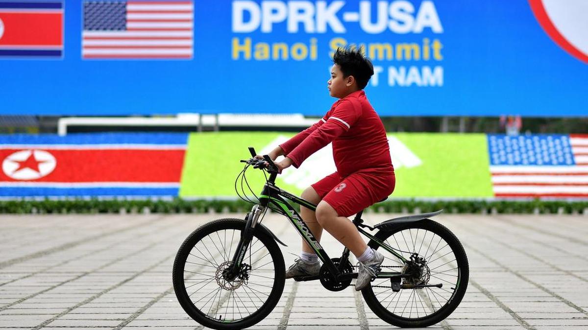 Un niño vietnamita pasa en bicicleta por una valla publicitaria para la próxima cumbre entre el presidente estadounidense Donald Trump y el líder norcoreano Kim Jong Un, en Hanoi, el 24 de febrero de 2019.