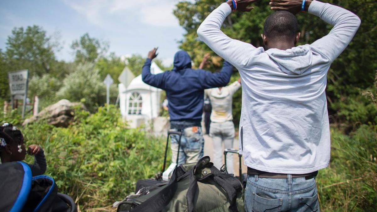 Un grupo de refugiados levanta sus manos antes de cruzar ilegalmente la frontera a Canadá desde Champlain, Nueva York el 4 de agosto de 2017.