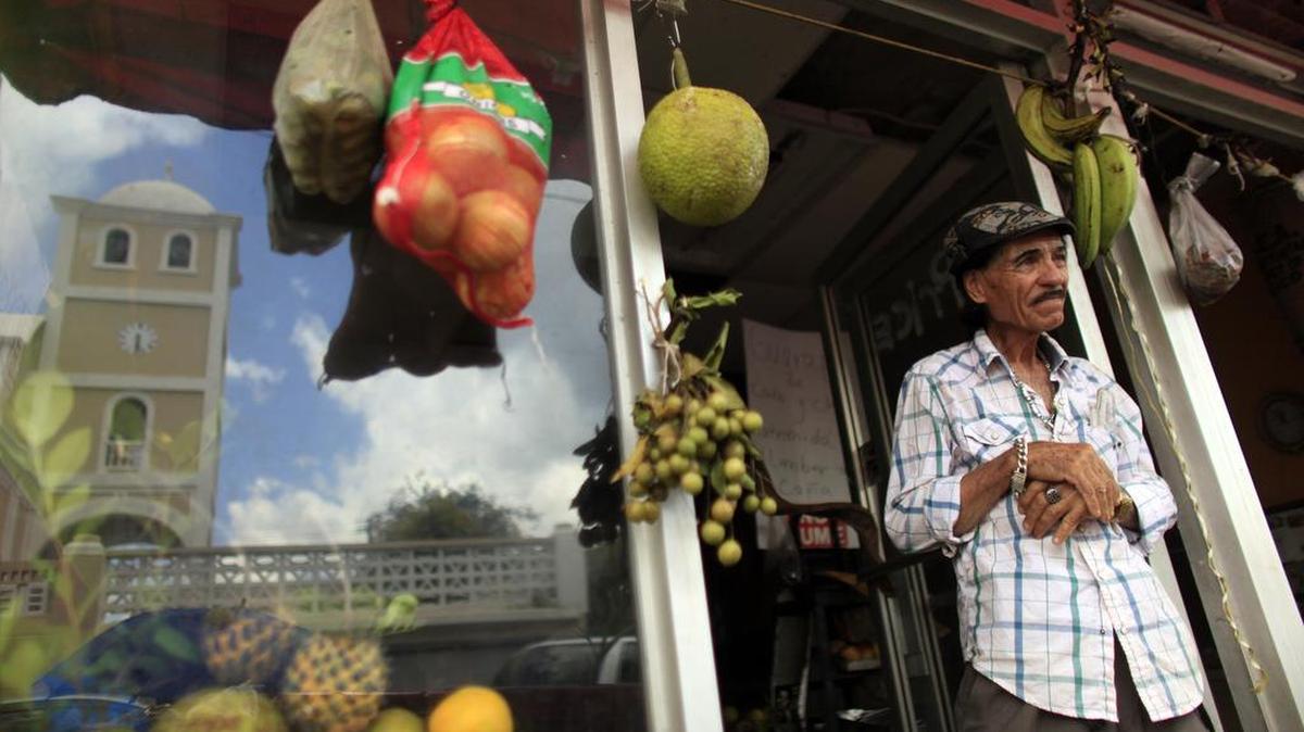 Angelo López, de 74 años, se encuentra frente a su tienda de fruta fresca en Lares, Puerto Rico. Lares se ha convertido en emblema del estancamiento económico que está abrumando Puerto Rico.