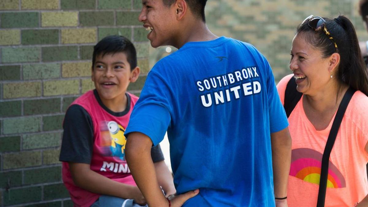 Un joven jugador de fútbol de Guatemala se ríe junto a su madre y su hermano menor durante una pausa en el partido en Macombs Dam Park el 22 de julio de 2017 en Nueva York.