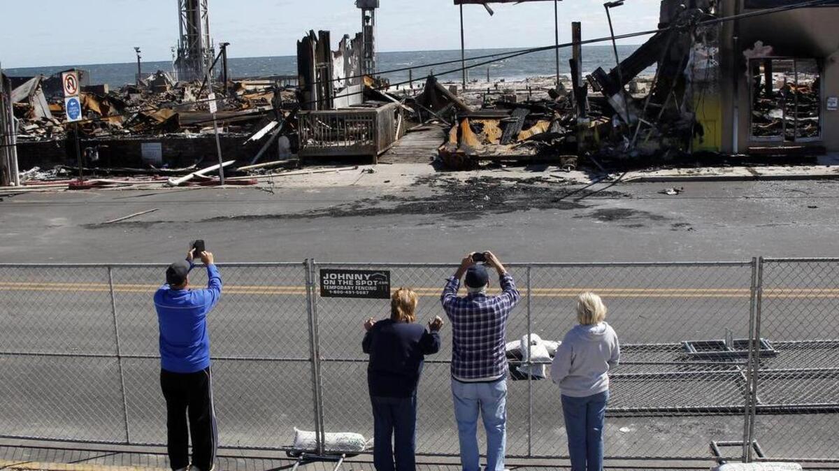 Un grupo de personas toman fotografías de los escombros carbonizados en Seaside Park, N. J. , martes , 17 de de septiembre de 2013, después del incendio que comenzó cerca de un puesto de crema helada en Seaside Park.