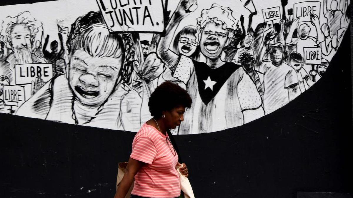 Esta foto de archivo tomada el 16 de mayo de 2017 muestra a una mujer puertorriqueña caminando frente a murales de protesta en San Juan, Puerto Rico.