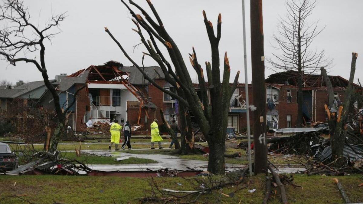 Vecinos y trabajadores de emergencias pasan junto a árboles afectados por un tornado junto a un complejo residencial en Garland, Texas, este domingo.