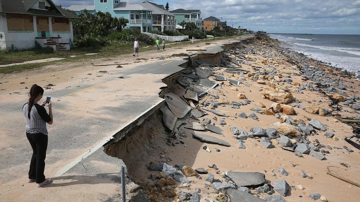 Una mujer, parada sobre lo que queda de la carretera A1A eb flagler Beach, florida, toma una foto de la playa erosionada por el huracán Matthew.