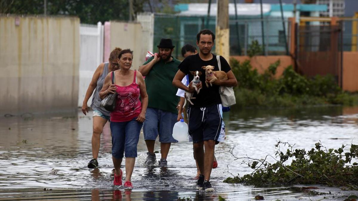 Unas personas caminan por una calle inundada por el paso del huracán María el jueves 21 de septiembre de 2017, en la municipalidad de Toa Baja en Puerto Rico.