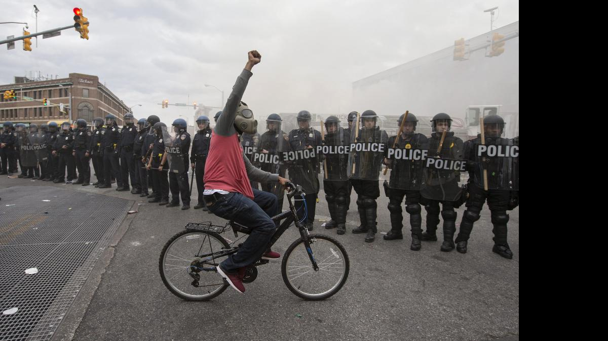 
Un hombre monta bicicleta frente a una barrera de policías durante una protestas por la muerte de Freddie Gray, en Baltimore (EE.UU.). Freddie Gray murió el 19 de abril después de sufrir una herida en su médula espinal mientras permanecía en custodia policial. La muerte de Gray motivo protestas y enfrentamientos con la policía, además de docenas de personas detenidas durante el fin de semana.

