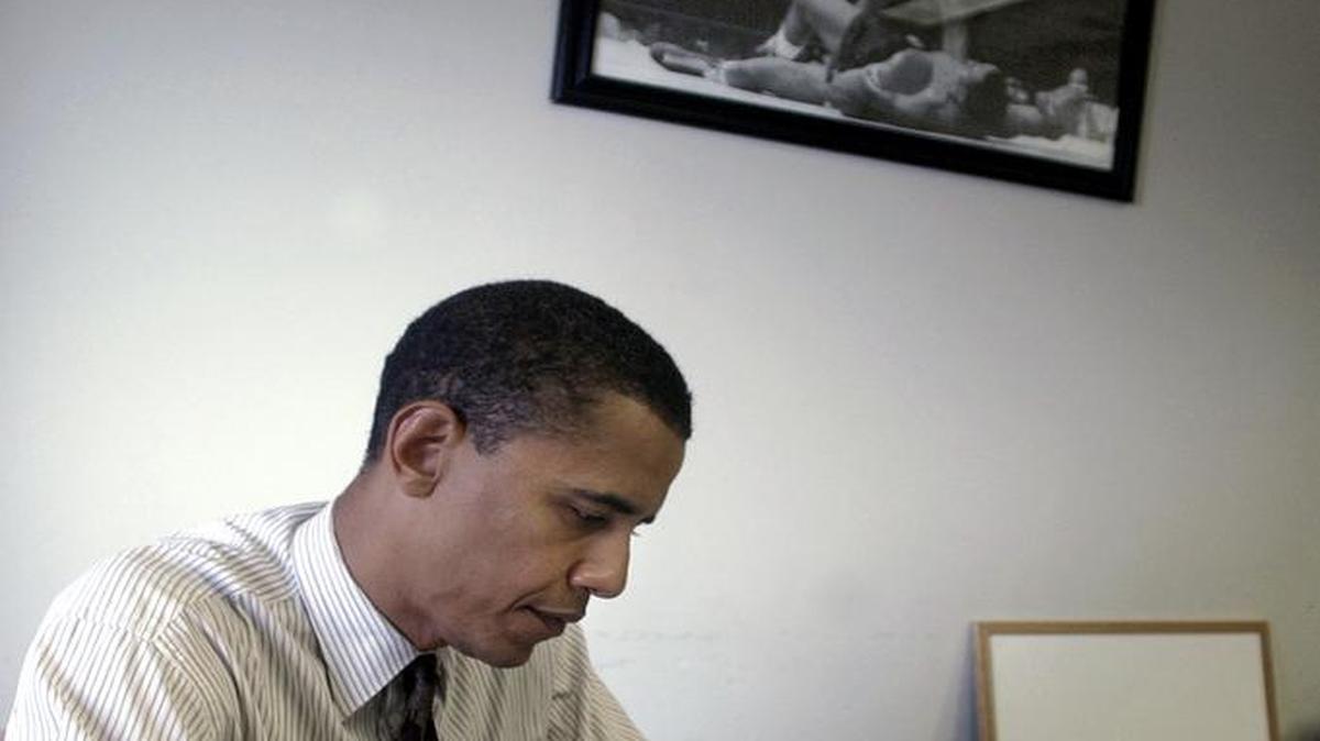 En esta foto de 22 de julio de 2004, el entonces candidato Barack Obama, trabaja cerca de una foto de un victorioso Muhammad Ali de pie.