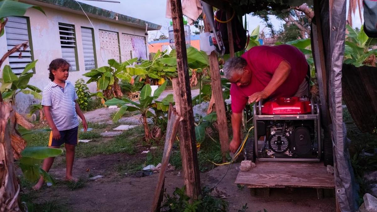 Julio Ortiz, de 7 años, observa a su padre, Angel Ortiz, de 47 años, encender un generador al atardecer. Su casa en Punta Santiago, Puerto Rico, se inundó hasta el pecho y la familia apenas escapó. Ahora están durmiendo en una tienda de campaña en el camino de entrada porque la casa está infestada de moho y mosquitos.