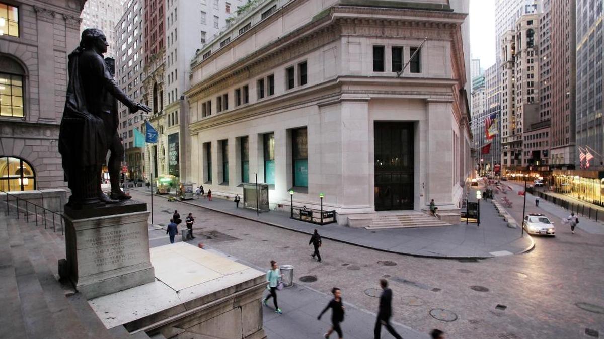 En esta foto de archivo del 8 de octubre de 2014, la gente camina a trabajar en Wall Street debajo de una estatua de George Washington, en Nueva York. Los mercados bursátiles mundiales subieron el lunes 16 de octubre de 2017, después de que líderes de finanzas globales apelen en una reunión de fin de semana del Fondo Monetario Internacional para continuar con políticas de bajas tasas de interés para mantener las recuperaciones económicas en camino.