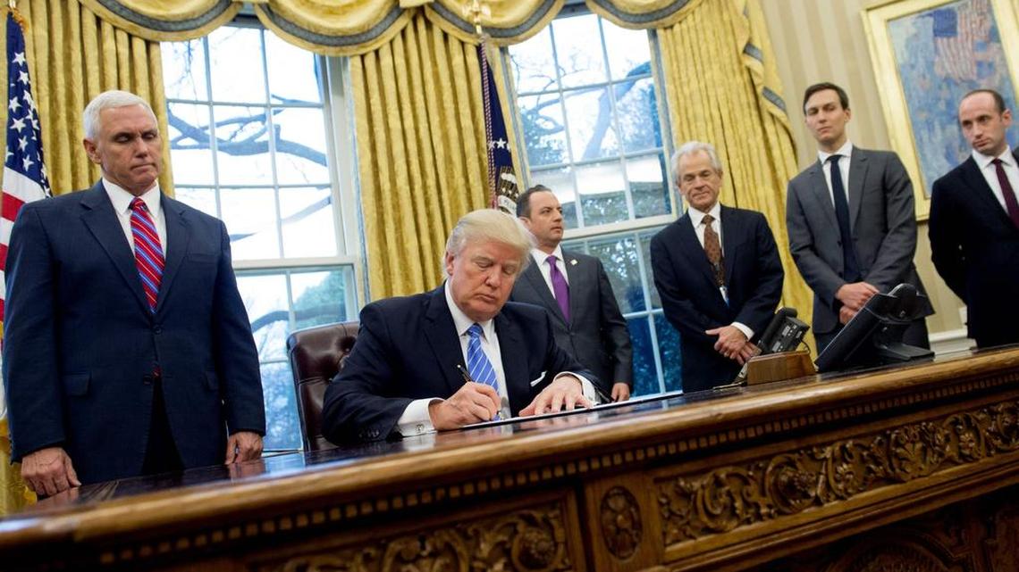En esta foto del 23 de enero de 2017, el presidente Donald Trump firma una orden ejecutiva acompañado del vicepresidente Mike Pence, el jefe del Gabinete Reince Priebus, y los asesores Peter Navarro, Jared Kushner y Stephen Miller, en la Oficina Oval de la Casa Blanca, Washington D.C.