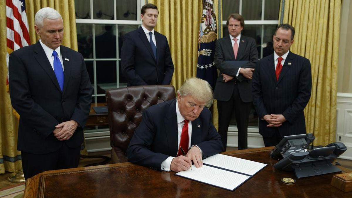 Foto del 20 de enero de 2017, el Presidente Donald Trump, acompañado por el Vicepresidente Mike Pence y el Jefe de Gabinete Reince Priebus, firma su primera orden ejecutiva sobre atención médica en la Oficina Oval de la Casa Blanca en Washington.