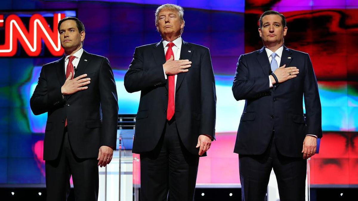 Los precandidatos Marco Rubio, izquierda, Donald Trump, (centro) y Ted Cruz, se llevan la mano al pecho durante el himno nacional al inicio del duodécimo debate republicano en la Universidad de Miami. Abajo, Rubio y Trump en un momento del intercambio.