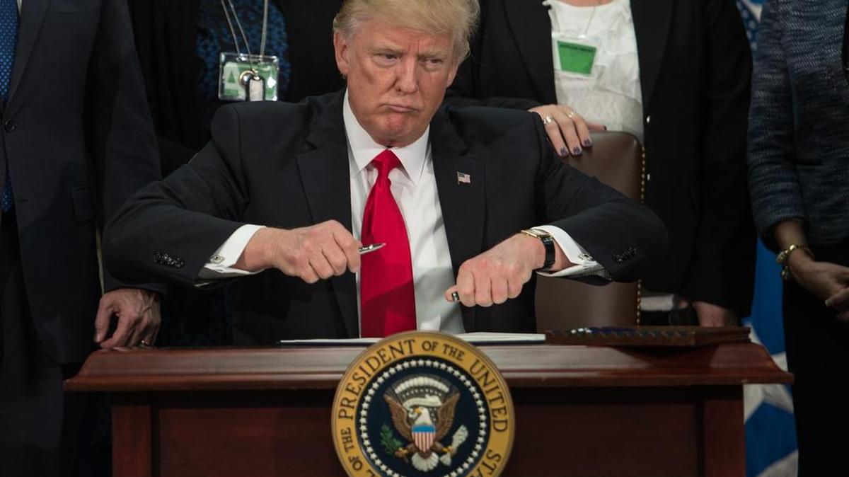 El presidente de los Estados Unidos, Donald Trump, saca la tapa de un bolígrafo para firmar una orden ejecutiva para iniciar el proyecto de la muralla fronteriza de México en el Departamento de Seguridad Nacional en Washington, DC, el 25 de enero de 2017.