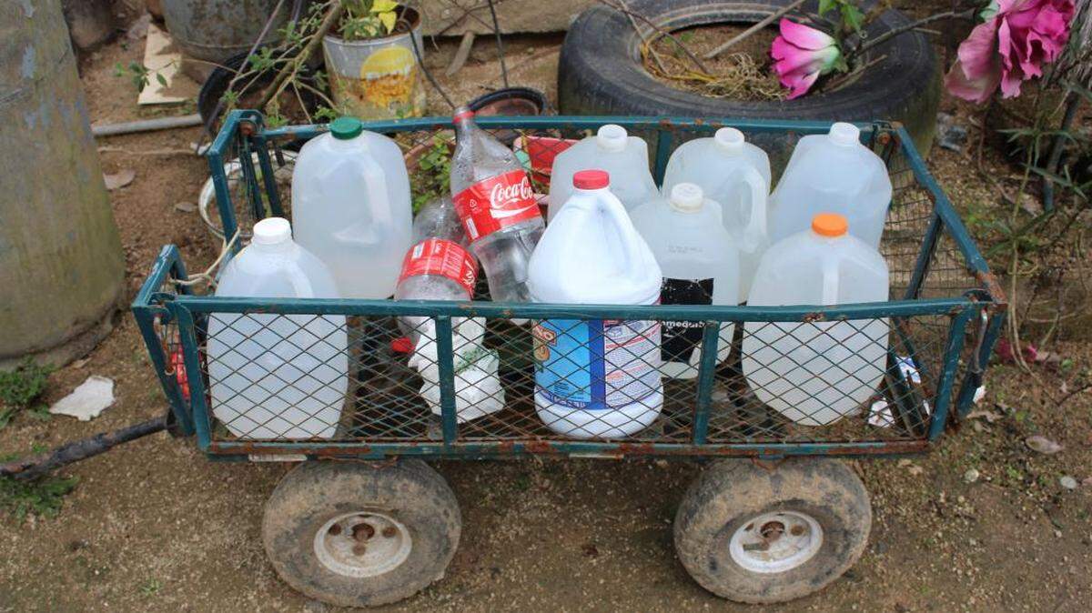 Elba Negrón Carreras utiliza botellas de plástico y leche para cargar agua. Ella y sus dos hijos deben caminar media hora hasta una estación para llevar a casa agua potable para cocinar, beber y hasta para ducharse.