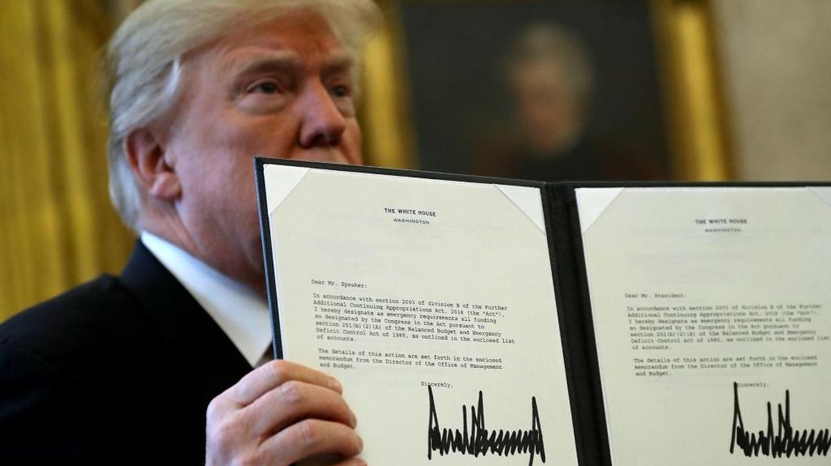El presidente Donald Trump muestra una copia del texto de la ley de reforma impositiva que suscribió el viernes en la Oficina Oval de la Casa Blanca.