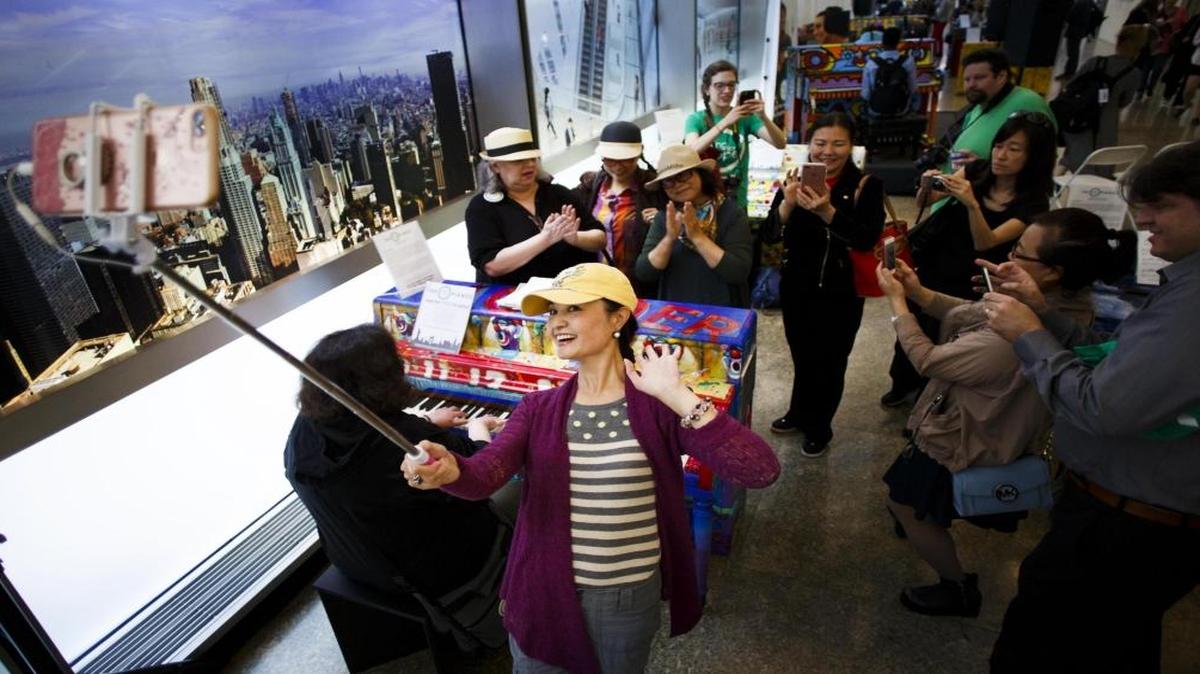 Turistas chinos posan junto a una mujer que toca uno de los 60 pianos que se dispondrán en diferentes áreas metropolitanas con motivo de la 6(TM) edición del programa "Sing for Hope" (canta por la esperanza) en Nueva York.