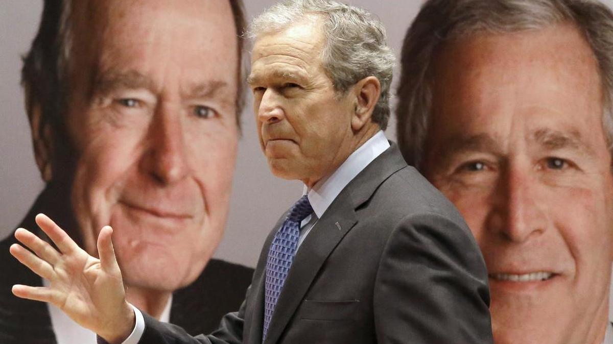 El ex presidente George W. Bush pasa frente a un retrato donde aparece él junto a su padre George H.W. Bush. 