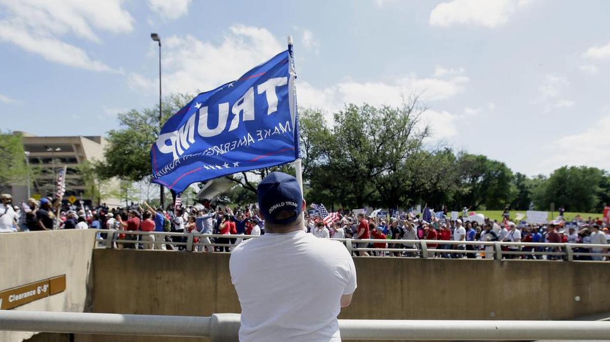 Dustin Marvin, seguidor del presidente Donald Trump, ondea una bandera mientras los manifestantes marchan por el centro de Dallas, el domingo 9 de abril de 2017.