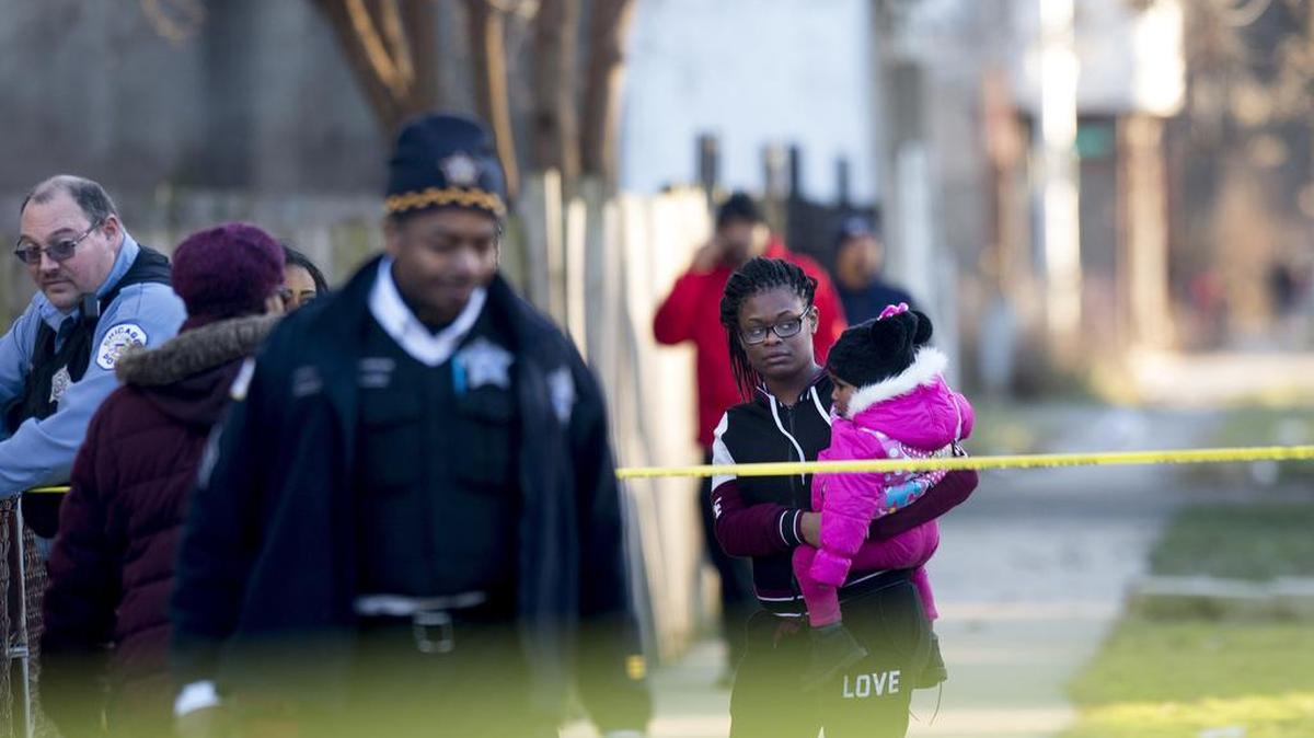 Una mujer que sostiene a un niño observa a los miembros del Departamento de Bomberos de Chicago transportando a una persona que fue disparada el lunes 26 de diciembre de 2016 en Chicago, Illinois.