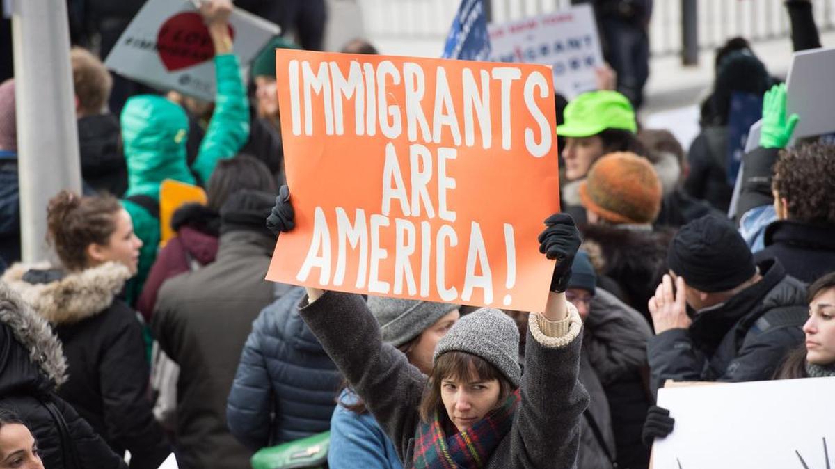 Miles de personas se reunieron el sábado en la Terminal 4 del Aeropuerto John F. Kennedy en Nueva York, para protesta la prohibición de entrada de refugiados y viajeros de siete países musulmanes. El aviso que sostiene la mujer en la foto dice “Los inmigrantes son América”.