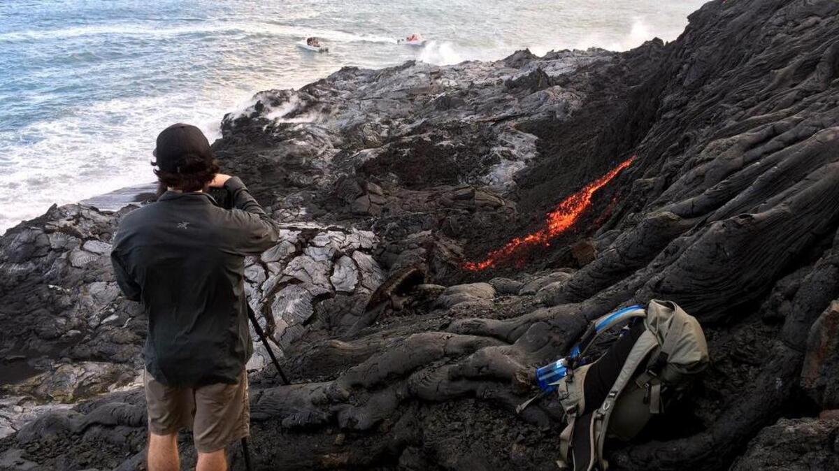 Un visitante hace fotos de una corriente de lava que fluye con lentitud desde el volcán Kilauea hacia el mar.