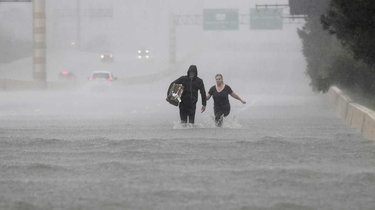 Dos personas caminan por una sección inundada de la Interstate 610 en medio de la tormenta tropical Harvey el domingo 27 de agosto de 2017 en Houston, Texas.