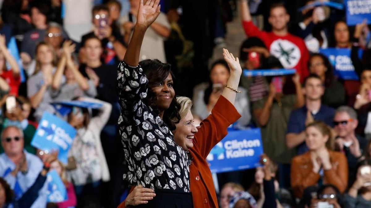La candidata a la presidencia de EEUU por el partido Demócrata Hillary Clinton (d) saluda junto a la primera dama, Michelle Obama (i) al cierre de un acto de campaña el jueves 27 de octubre 2016, en el Coliseo del Centro de Veteranos Lawrence Joel en Winston-Salem.
