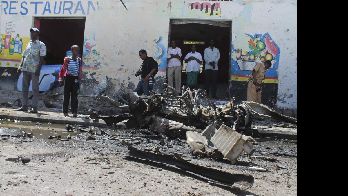 
Un agente de seguridad (der.), varios vecinos y un periodista (3 izq.). permanecen en el lugar en el que se registró la explosión de un coche bomba a las puertas de un restaurante de Mogadiscio, Somalia, el martes.


