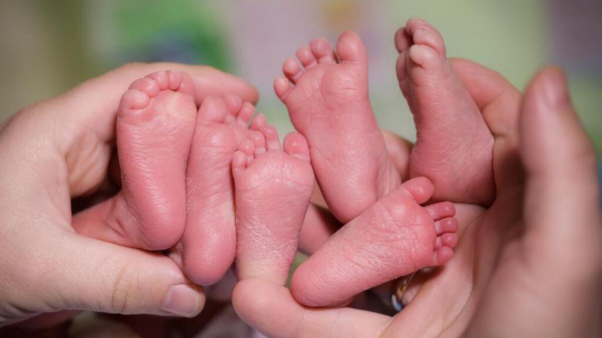 Una madre sostiene los pies de sus tres recién nacidos.