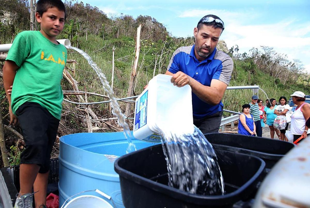 Robert Rodríguez (izquierda) y José Méndez recogen agua que baja de la montaña junto a una carretera en el poblado de Utuado, Puerto Rico.