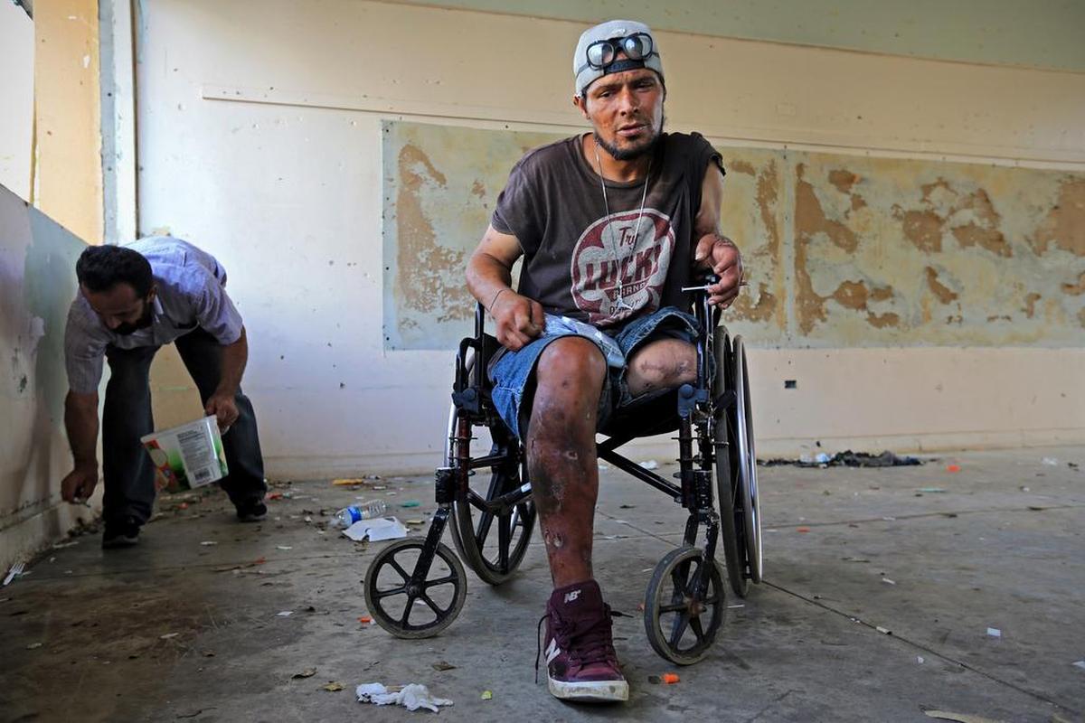 Oliver Franco Rivero sostiende una jeringuilla antes de inyectarse heroína y cocaína en una escuela abandonada en Cidra, Puerto Rico, el 19 de octubre. A la izquierda, Luis Manuel Quiles Santos recoge jeringuillas sucias para cambiarlas por nuevas con la organización Mountain Point. Esta organización no gubernamental ofrece a los participantes jeringuillas nuevas, educación sobre la reducción de riesgos, así como alimentos y artículo de higiene personal y de primer auxilio.