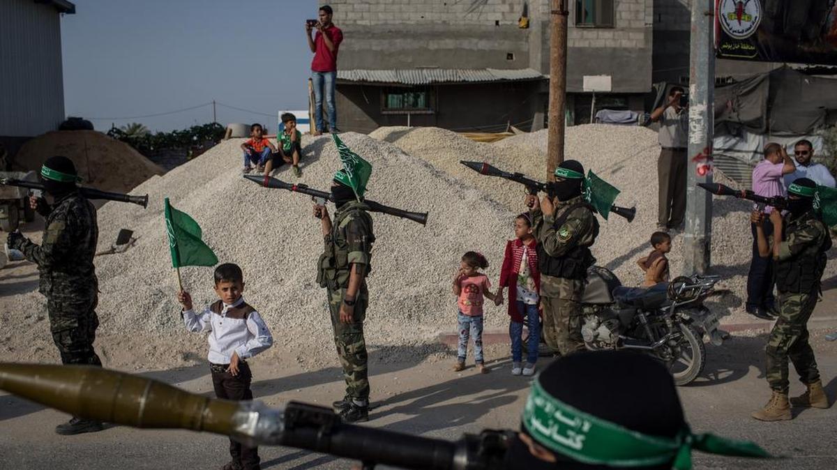 Un niño sostiene una bandera de Hamas junto a militantes palestinos, durante un espectáculo militar en el distrito de Bani Suheila, en la ciudad de Gaza.
