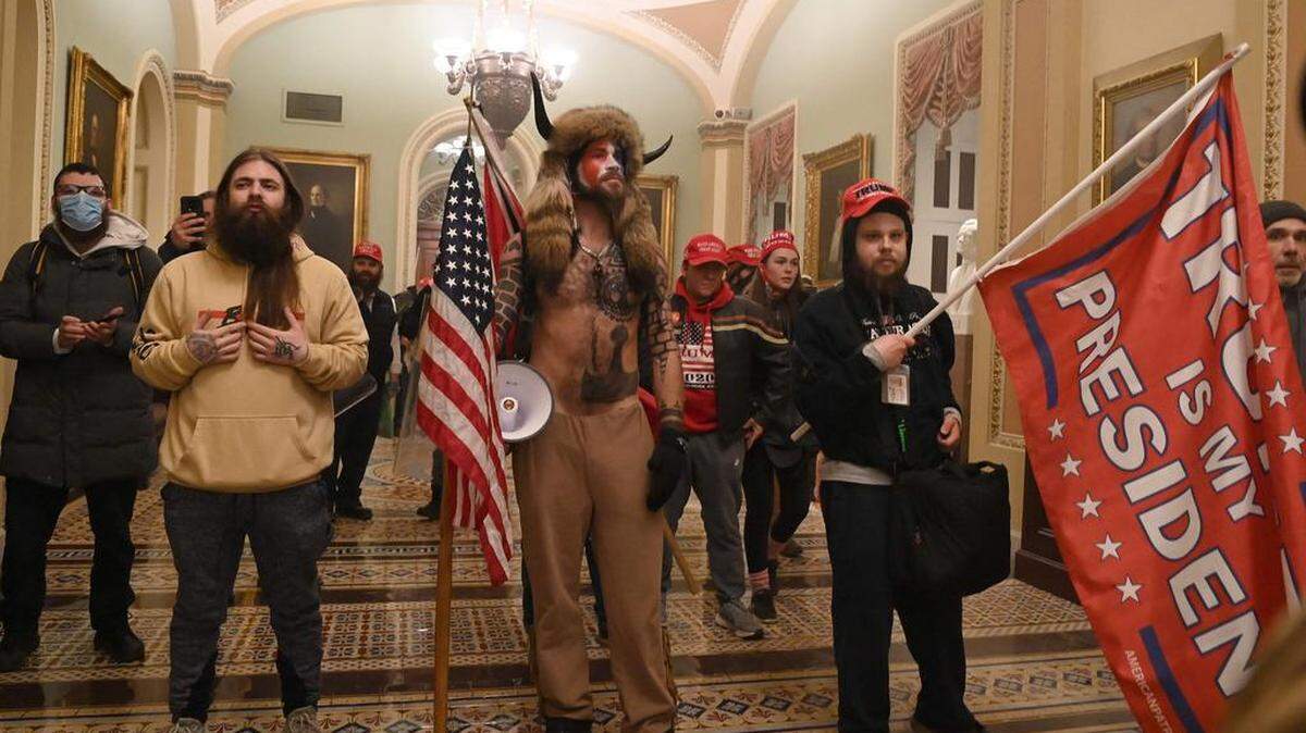 (ARCHIVO) En esta foto de archivo tomada el 6 de enero de 2021, partidarios del presidente de los Estados Unidos, Donald Trump, incluido el miembro del grupo conspirativo de QAnon, Jake Angeli, también conocido como Yellowstone Wolf (C), ingresan al Capitolio de los Estados Unidos en Washington, DC. - Un año después de que los partidarios de Donald Trump irrumpieran en el Capitolio de los Estados Unidos y cerraran el Congreso, los estadounidenses aún esperan un ajuste de cuentas sobre el desafío sin precedentes a la democracia del país. ¿Fue una simple protesta convertida en disturbios? ¿Una insurrección? ¿Un intento de golpe tramado por Trump? Los videos del 6 de enero de 2021 dan testimonio de la violencia ejercida en nombre del expresidente. Atacantes golpeando a los agentes de seguridad con barras y palos de hierro. Un policía aplastado en una puerta, aullando de dolor. Los alborotadores vestidos con equipo de asalto coreando “Hang Mike Pence”, mientras el vicepresidente y los legisladores demócratas y republicanos huyen. Una mujer asesinada a tiros en un pasillo del Capitolio. Los estadounidenses quedaron atónitos por el asalto que duró horas, y también gran parte del mundo, acostumbrado a ver a Estados Unidos como un modelo de democracia estable. (C)