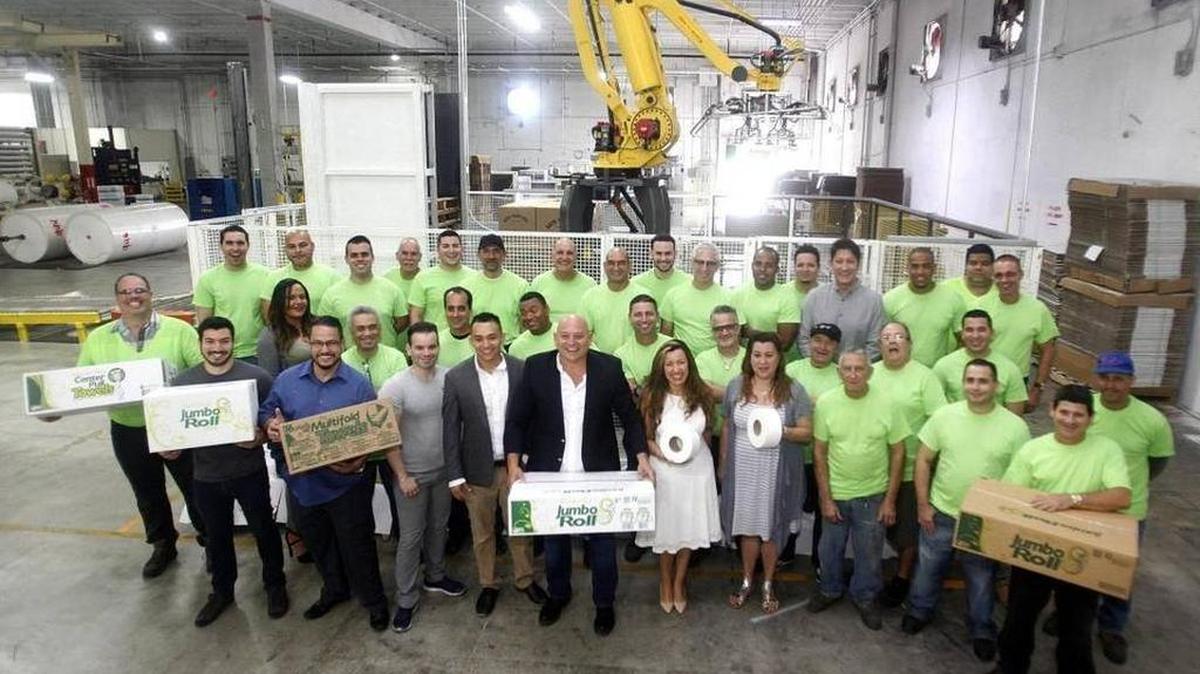 Juan Corzo, CEO de South Florida Tissue Paper Co (cen. de chaqueta negra) posa con varios de los empleados en la sede de la empresa.