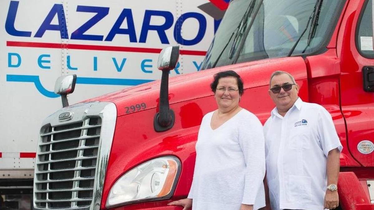Marlene Pérez y su esposo Lázaro Ramos, copropietarios de Lázaro Delivery, posan con varios de sus camiones en la sede de la empresa, en Miami.