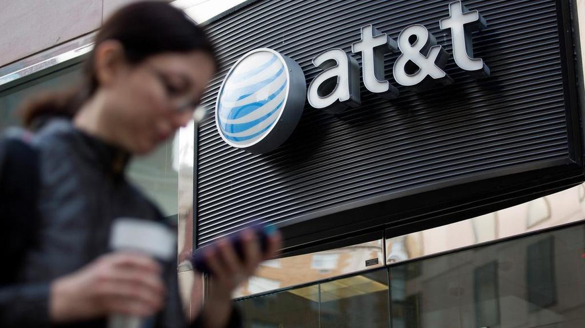 Un peatón mira su teléfono móvil mientras pasa frente a una tienda de AT&T Inc. en Washington, D.C., el 23 de octubre del 2014.