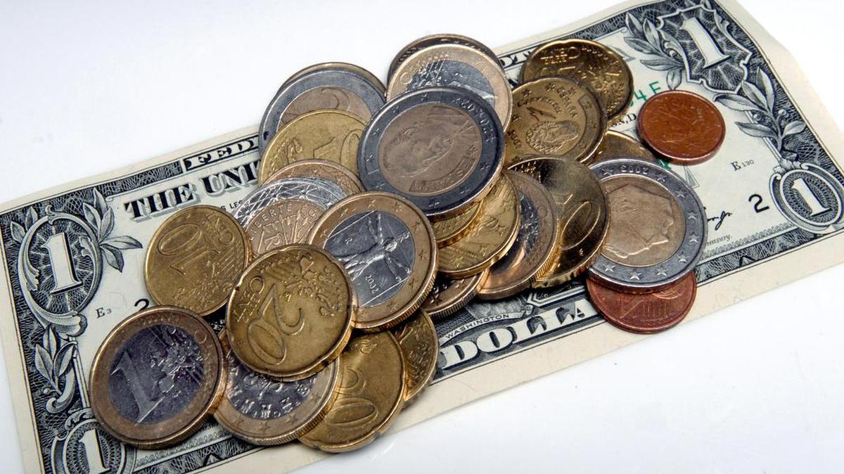 Un billete de un dólar bajo una pila de monedas de euro.