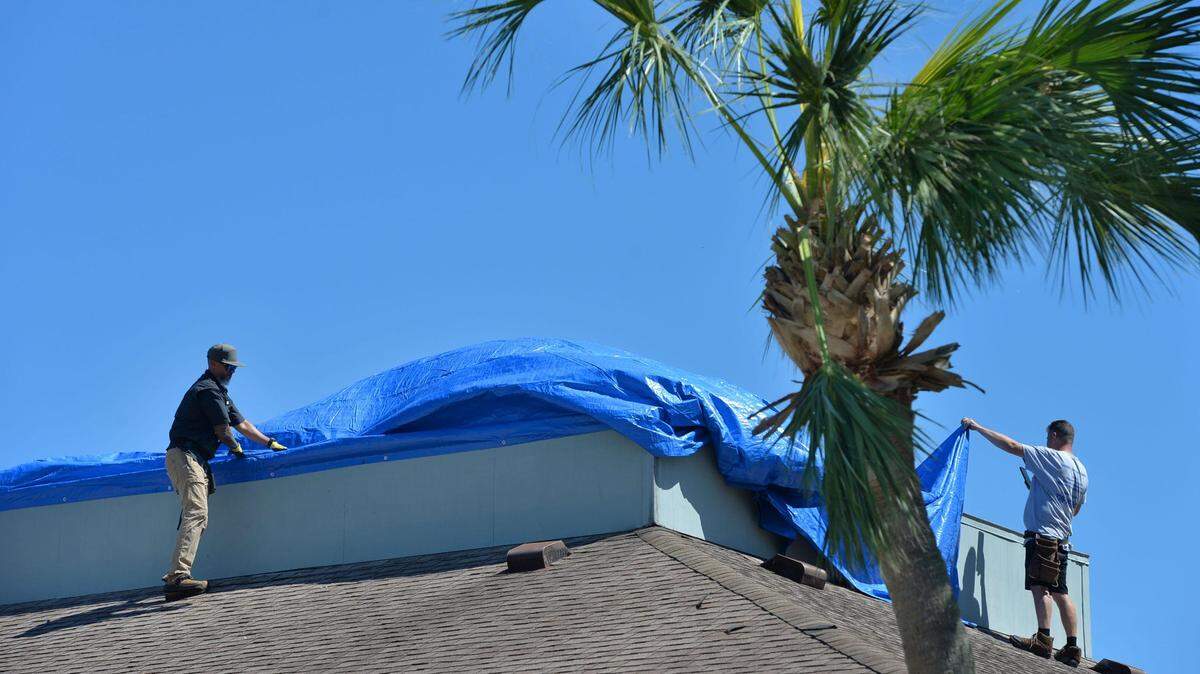 Trabajadores colocan un toldo azul para proteger el techo de un negocio afectado por el impacto del huracán Ian, en Punta Gorda, Florida, el viernes 30 de septiembre de 2022.