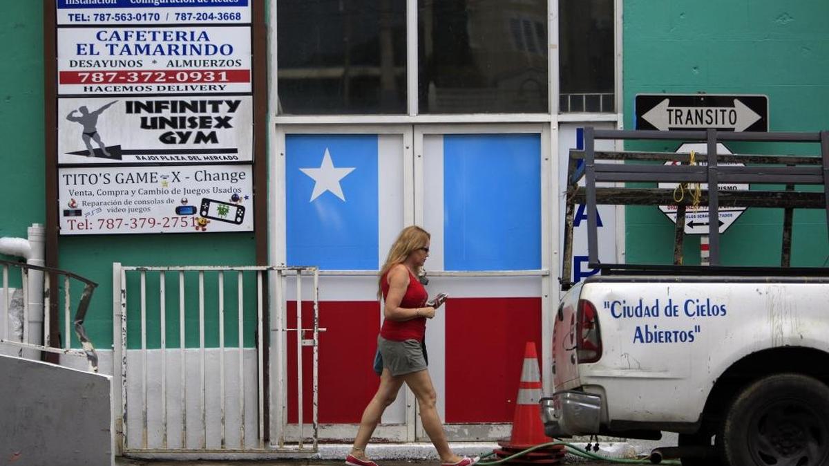 Una mujer pasa frente a un negocio en Lares, Puerto Rico. La Asociación de Constructores de Puerto Rico (ACPR) presentó el jueves propuestas de desarrollo económico para poner fin a la crisis.
