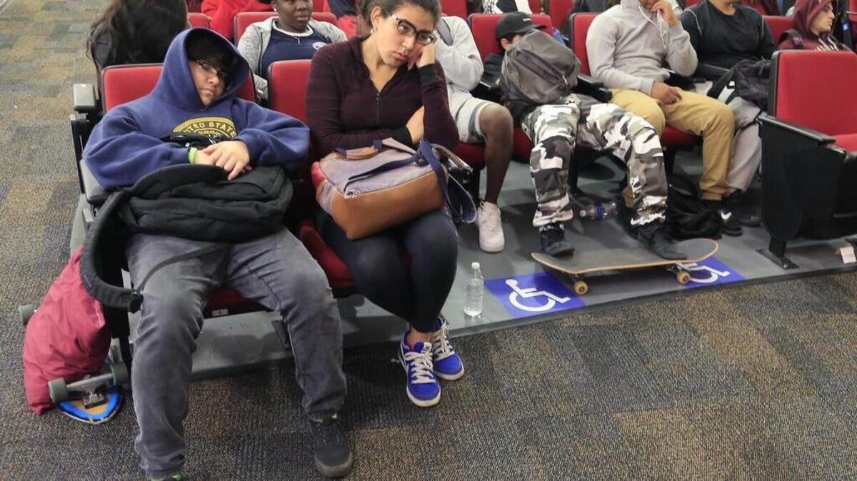 Tony López, de 18 años, duerme en su asiento, mientras Jennifer Acevedo, 18, escucha lo dicho en el programa de educación financiera de la SEC en una escuela secundaria de Miami.
