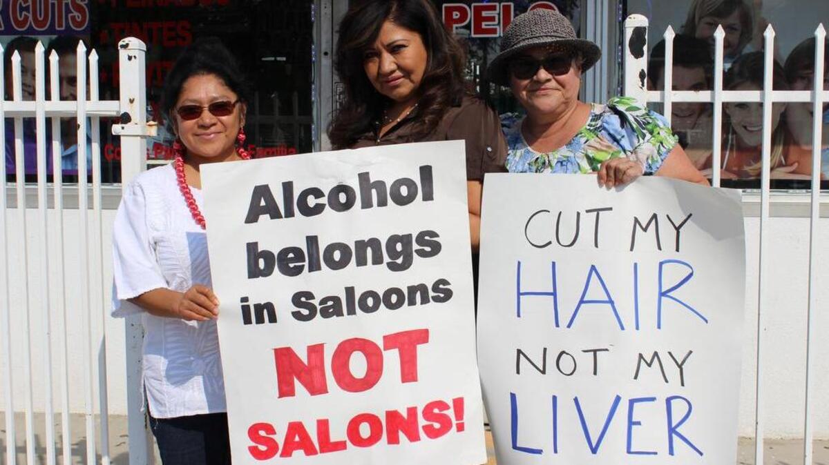 De izq. a der., los activistas Virginia Megerdichian, Lupita Macías y Toni Joseph protestan con pancartas que dicen: "El alcohol en los bares, no en los salones de belleza" y "Corta mi cabello, pero no mi hígado", frente a la peluquería de Macias en San Fernando, California.