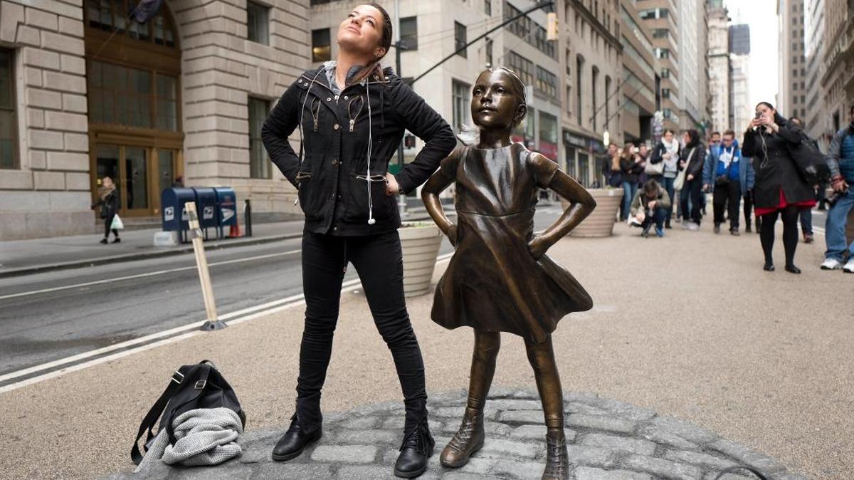 Una mujer posa junto a una estatua titulada “Fearless Girl” (Niña sin miedo) en Nueva York.