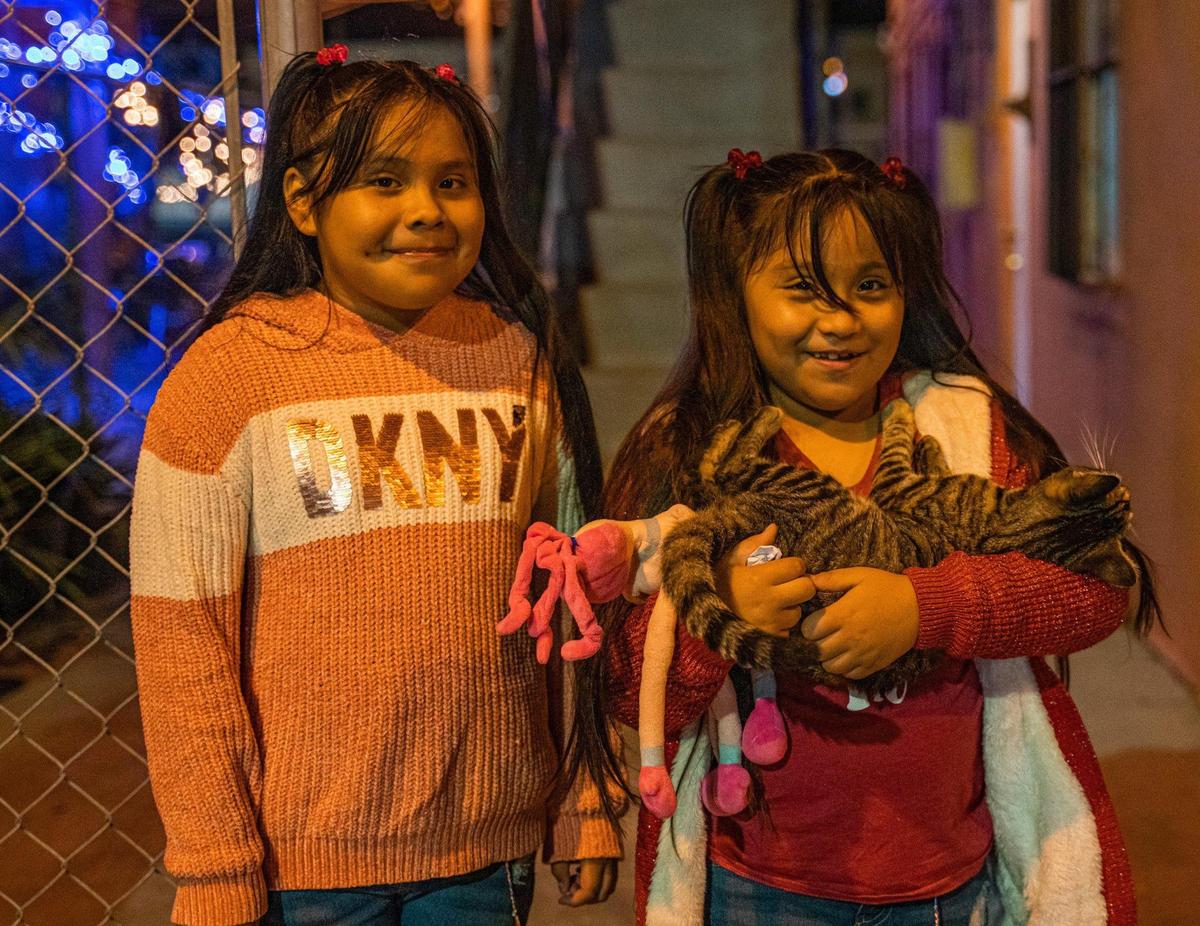 Brenda and Abigail Arreguín pose with a cat by the building where they live in Homestead. The girls need clothes, shoes and other items that their father can’t afford to buy with his low wages.