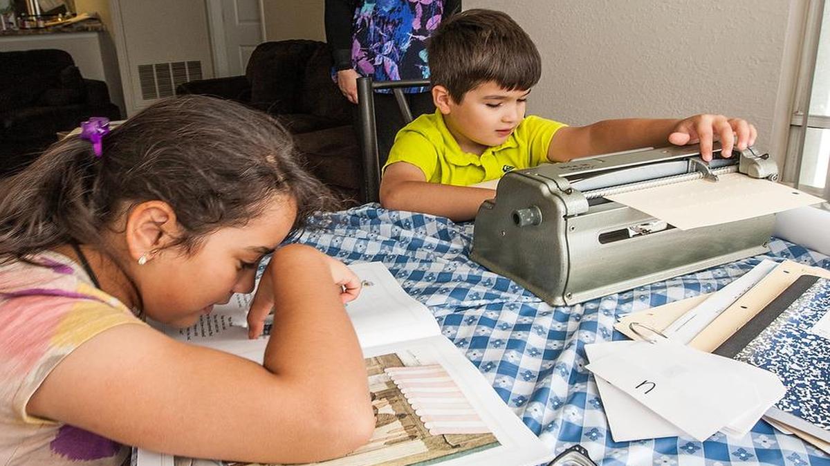 Aref Shabaneh (der.) y su hermana Yasmeen Shabaneh hacen las tareas, mientras su madre, Reema Shabaneh, observa. Los dos niños, con graves problemas de la vida, works on his spelling assignment for his first grade class at Kate Sullivan School while his older sister , seated left, a 9 years old fourth grader, reads The Gingerbread Man at their home in Tallahassee, Florida October 28, 2015.. The two children - both of whom are mostly blind - were eliminated from a Florida state Department of Health's program in an effort to save money by cutting back dramatically on a taxpayer-funded program for the sickest and most disabled children, called Children's Medical Services, or CMS.With their mother in the background,